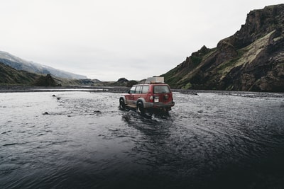 白天在山附近的水面上行驶的红色SUV